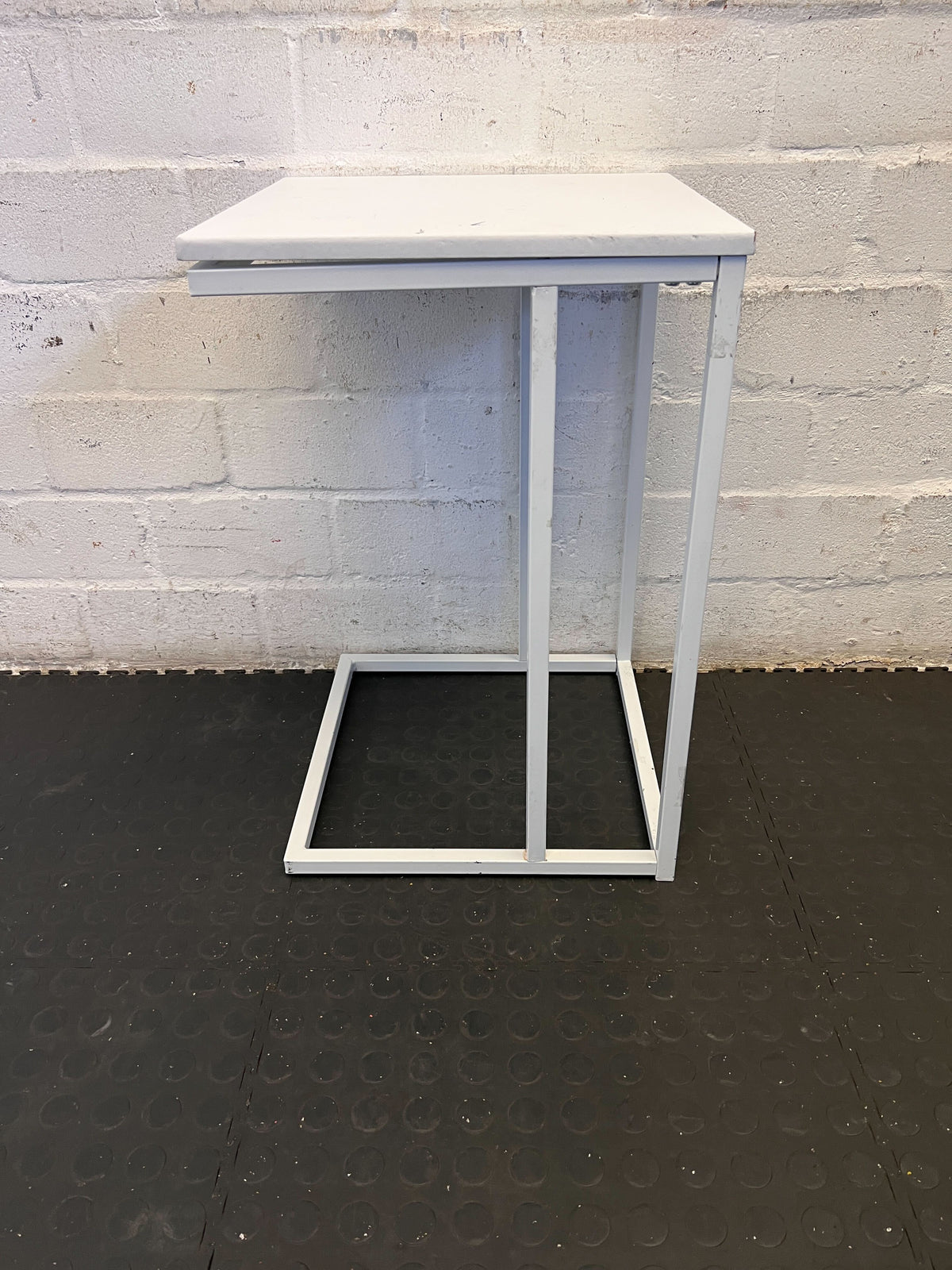 Small white table against a gray brick wall.