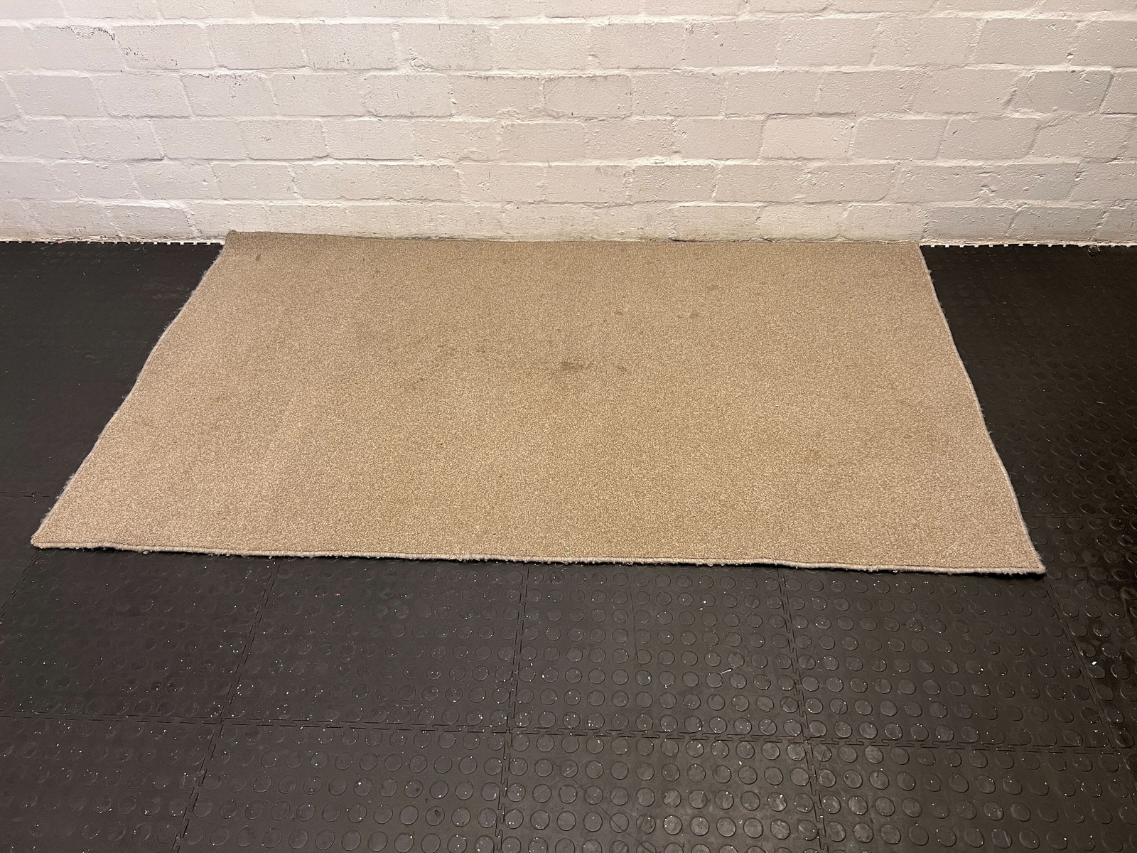 Brown mat on a black textured floor with a white brick wall background