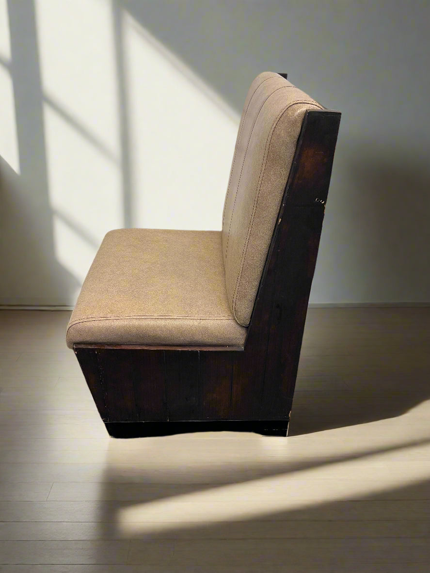 Beige cushioned chair against a white brick wall.