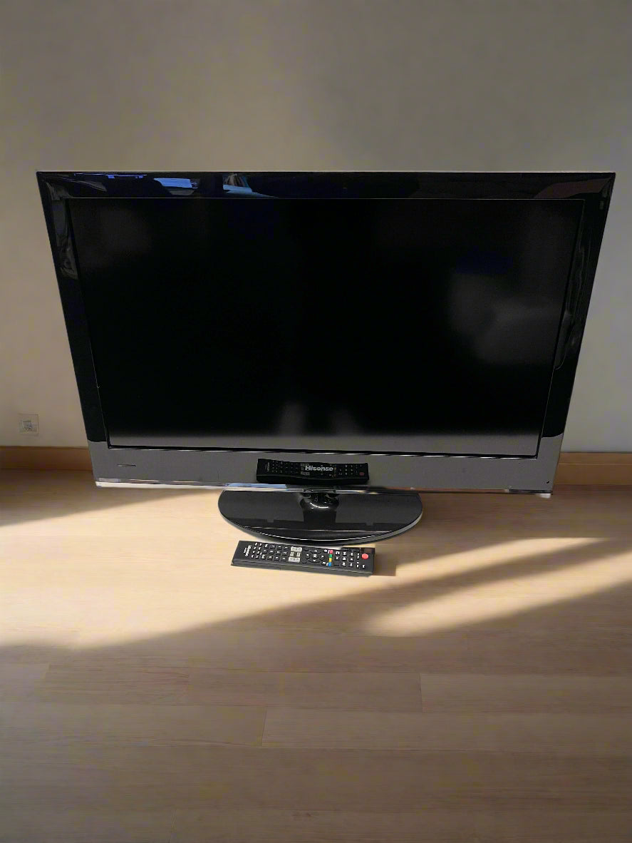 Black flat-screen TV on a wooden floor with a remote control in front