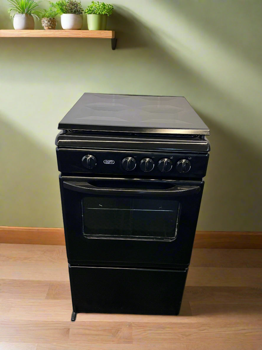 Black electric cooker on a wooden floor with a green wall and shelf in the background