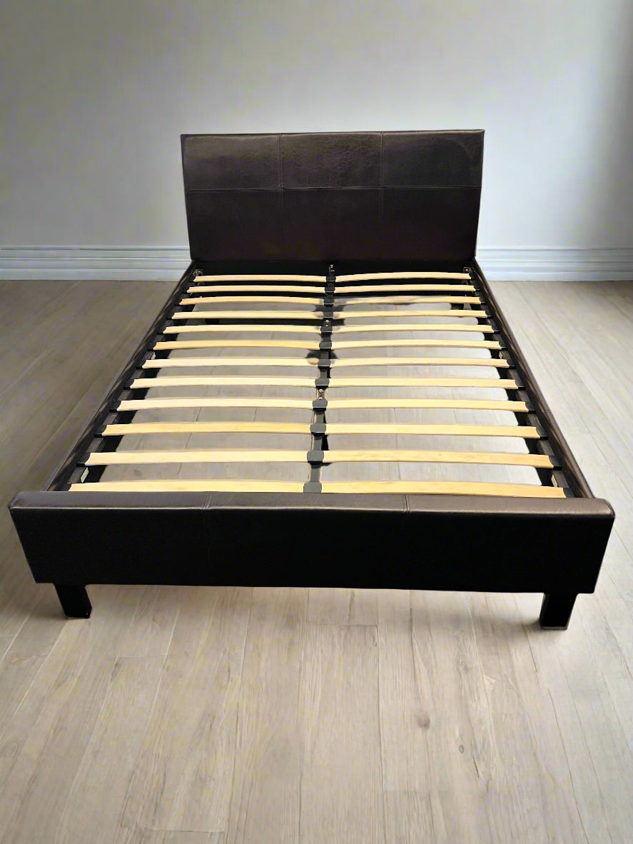 Black bed frame with wooden slats on a gray floor against a white brick wall.