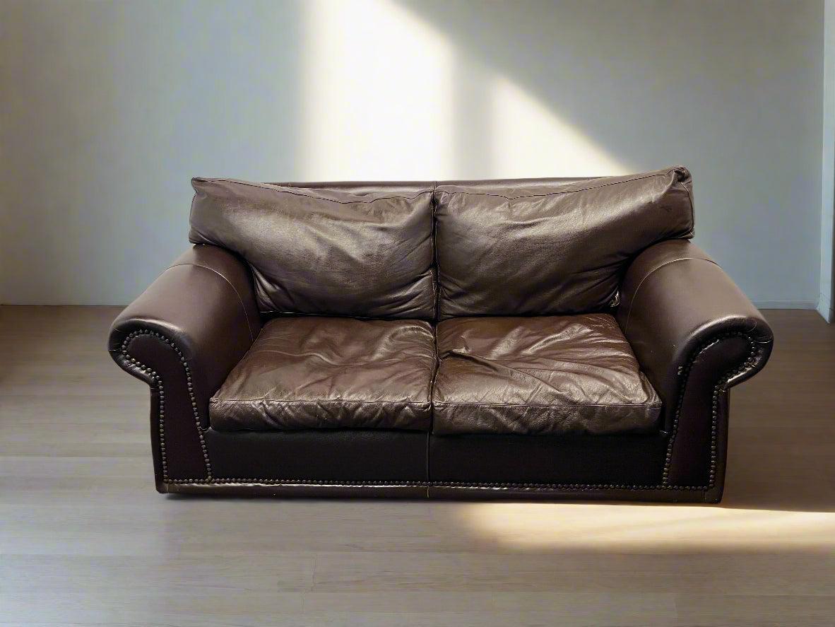 Brown leather sofa in a minimalistic room with light-colored walls and floor.