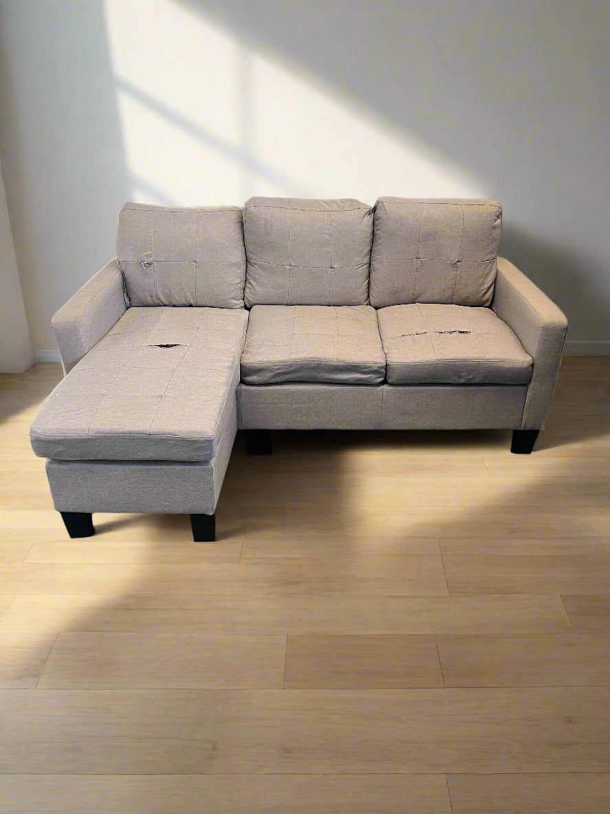 Gray sectional sofa in a room with wooden flooring and a white wall.
