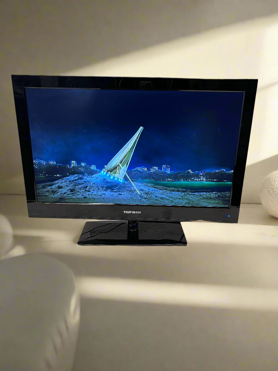 Black flat-screen TV on a white surface with a gray brick wall background