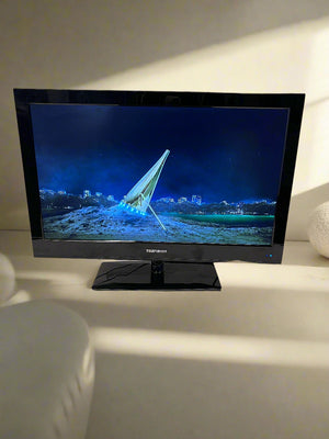 Black flat-screen TV on a white surface with a gray brick wall background