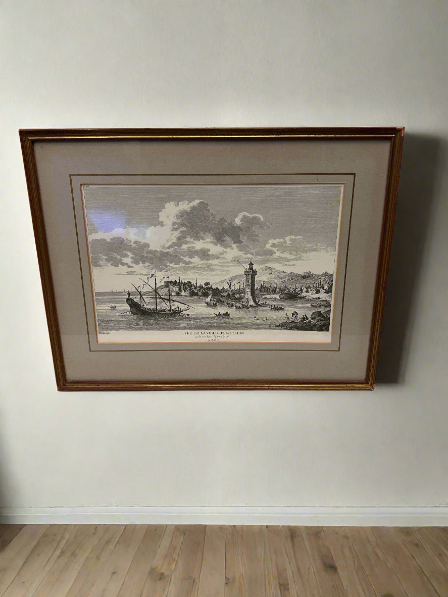 Framed black and white print of a coastal scene on a beige wall.