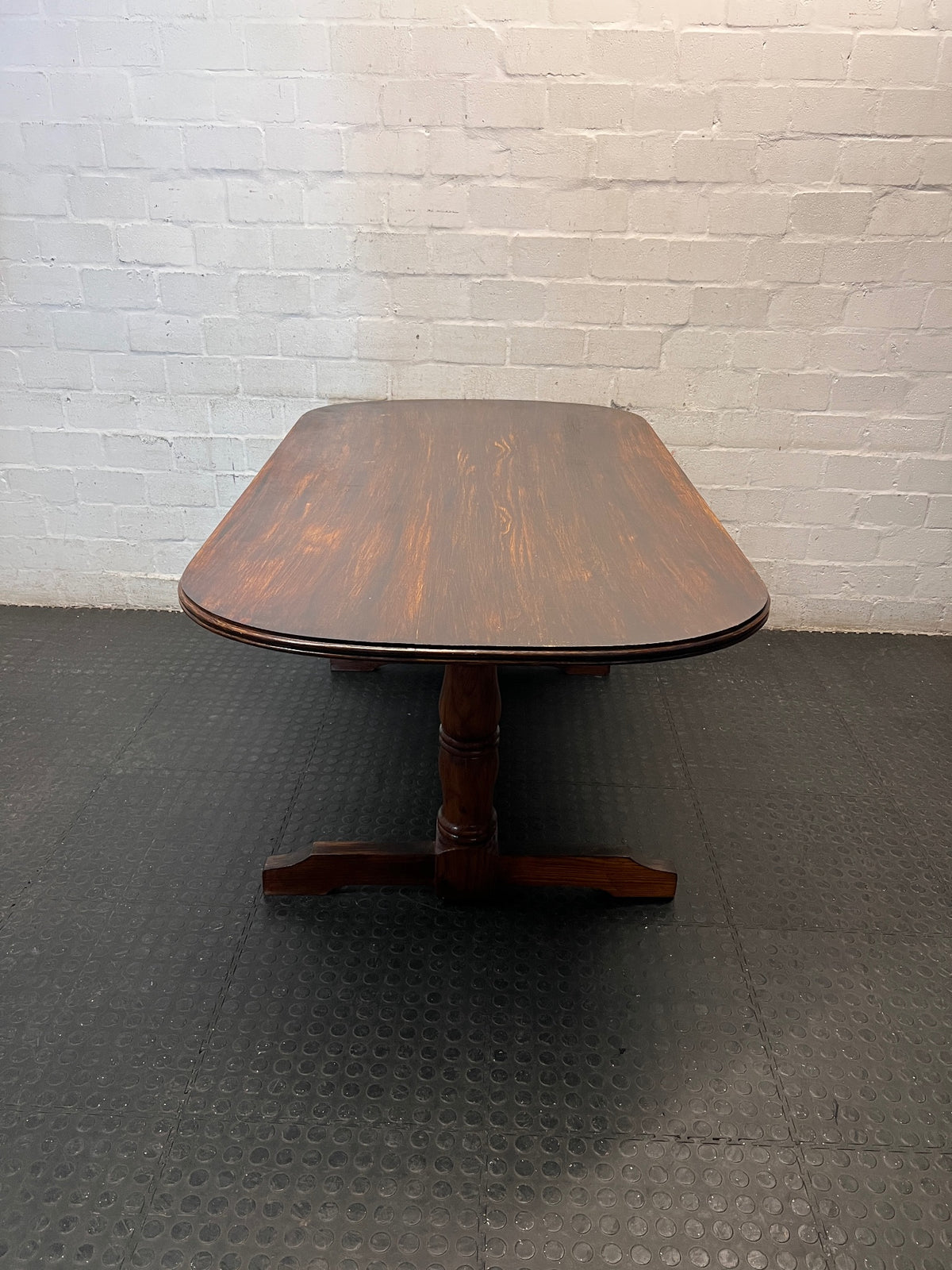 Rounded Brown Timber Dining Table with Pedestal Base — Visible Wear on Tabletop – side view